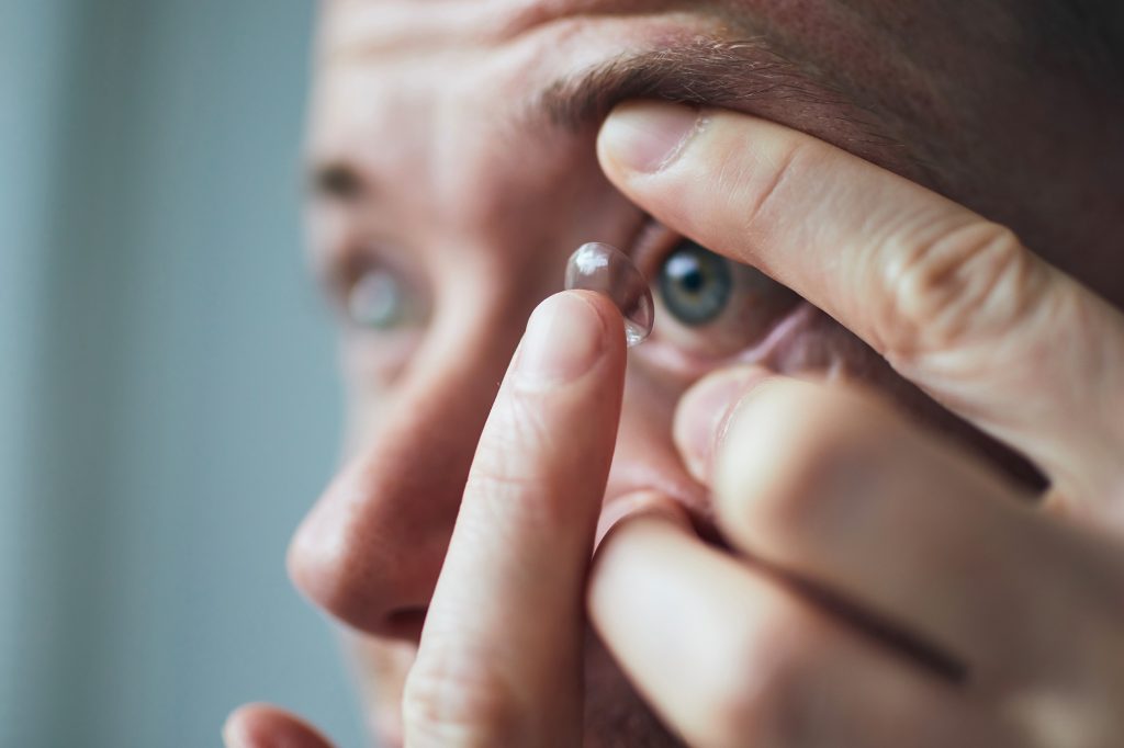 Young man putting contact lens on eye.