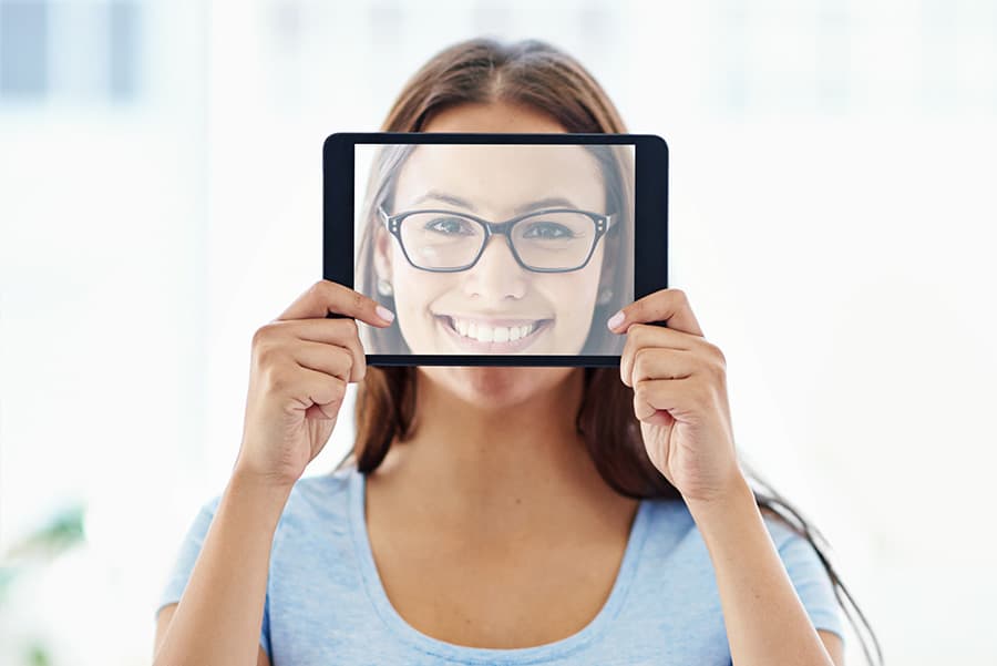 Pretty-brunette-wearing-glasses-holding-up-a-tablet-with-a-picture-of-her-face-on-the-screen.jpg